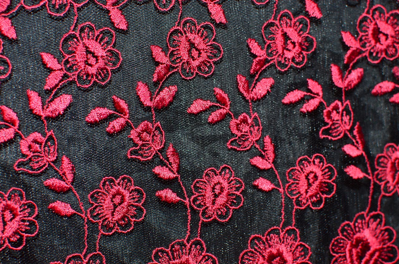 Seamless background of creative flowers with leaves embroidered on black fabric with red thread creating symmetrical pattern on thick textile